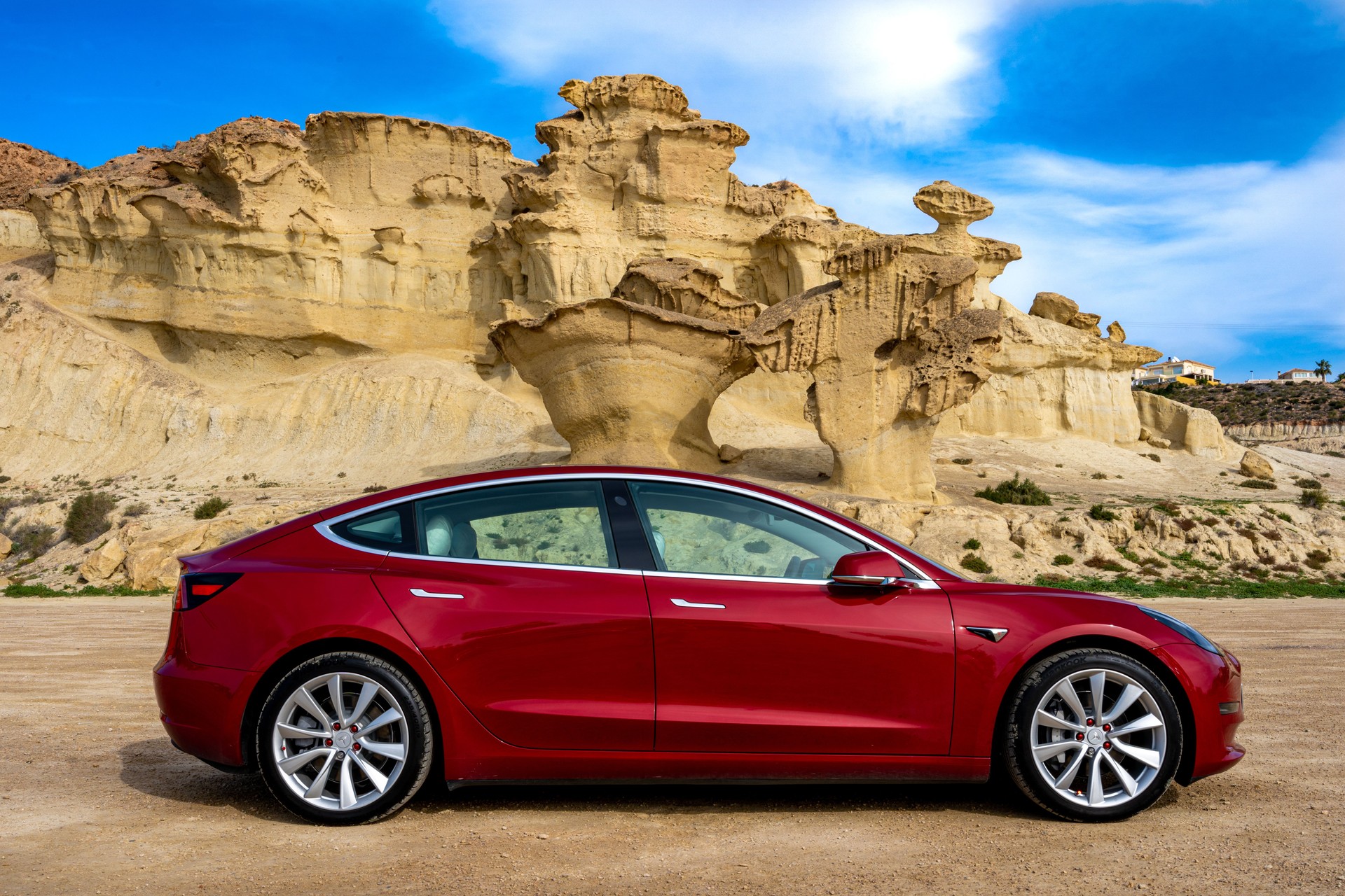 side view of a red Tesla Model 3 electric car with rock formation on the mediterranean coast and blue sky in Bolnuevo, Murcia, Spain.